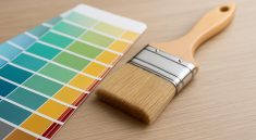 A paintbrush resting next to a color palette on a wooden surface.