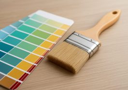 A paintbrush resting next to a color palette on a wooden surface.